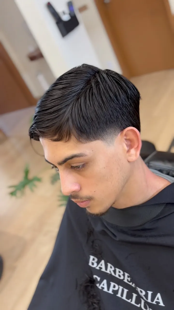 Cliente com franja e capa preta com o nome Barbearia Capillus