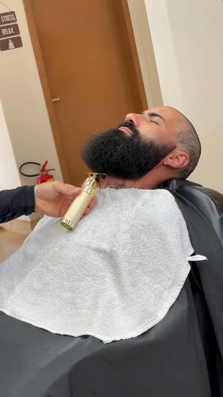 Barbeiro fazendo o acabamento de uma barba cheia com máquina dourada